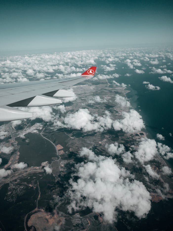 Scenic view of a coastline from an airplane window with scattered clouds.