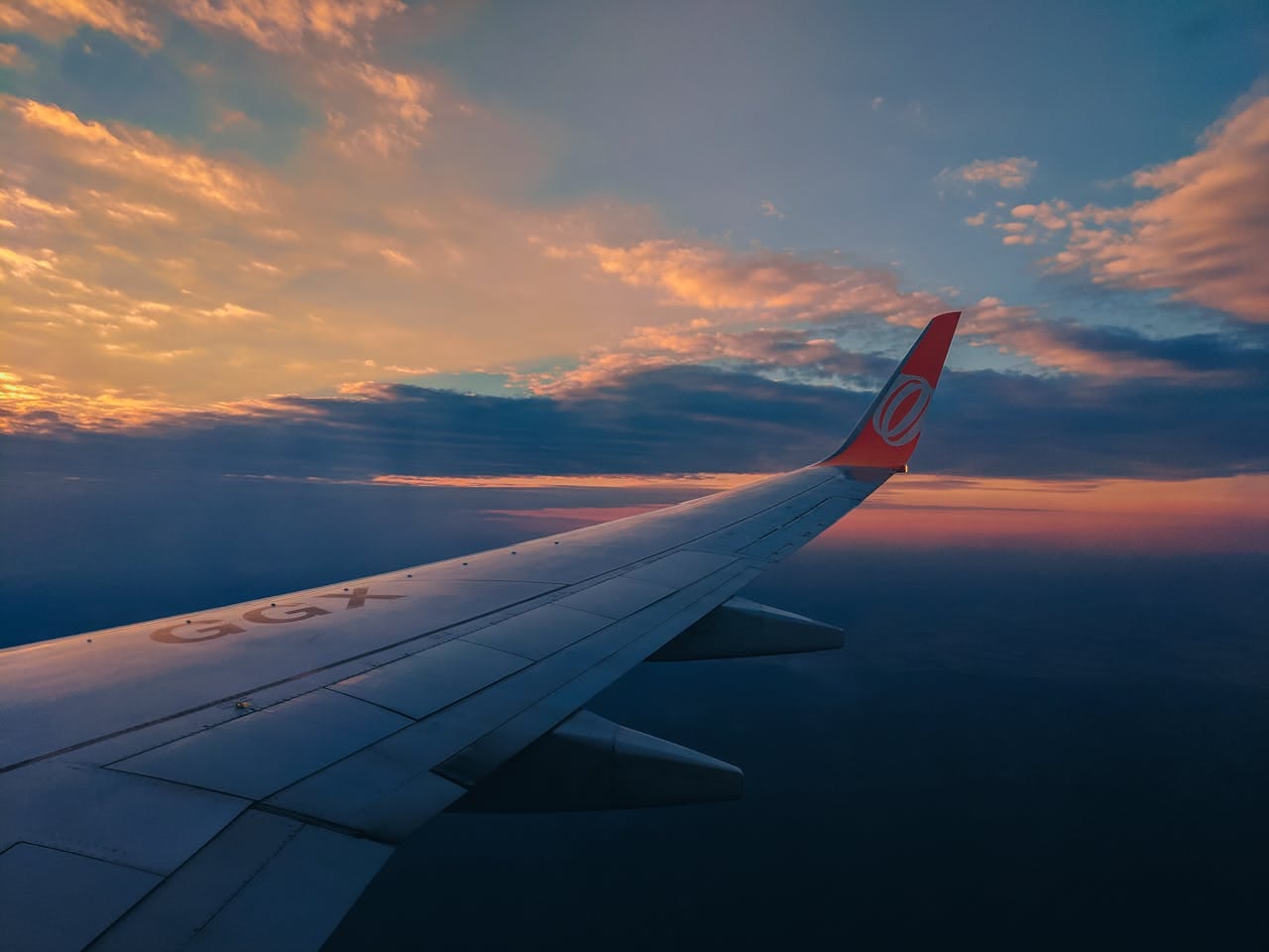 View of an airplane wing soaring above a vibrant sunrise cloudscape, emphasizing travel and adventure.